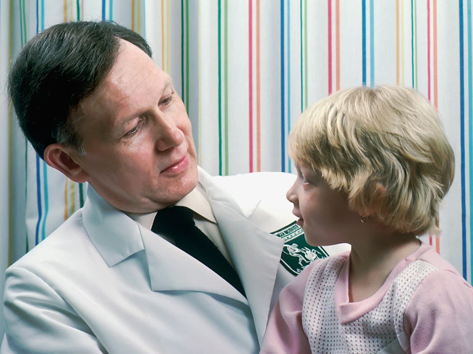 Profesional de la salud conversando de cerca con una niña en edad escolar durante una consulta pediátrica.